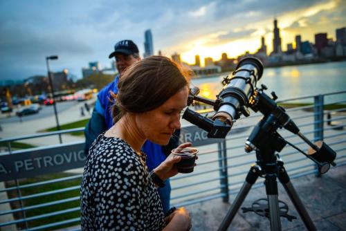 An image of an Adler guest peering out of a telescope on the Adler's terrace during an "Adler After Dark" event.