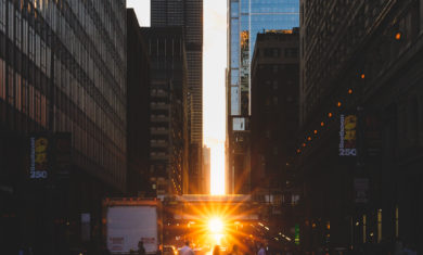 Pedestrians walking (during Chicagohenge) across a crosswalk while the Sun sets in the distance with the Willis Tower in view.