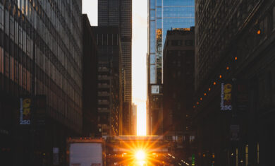 Pedestrians walking (during Chicagohenge) across a crosswalk while the Sun sets in the distance with the Willis Tower in view.