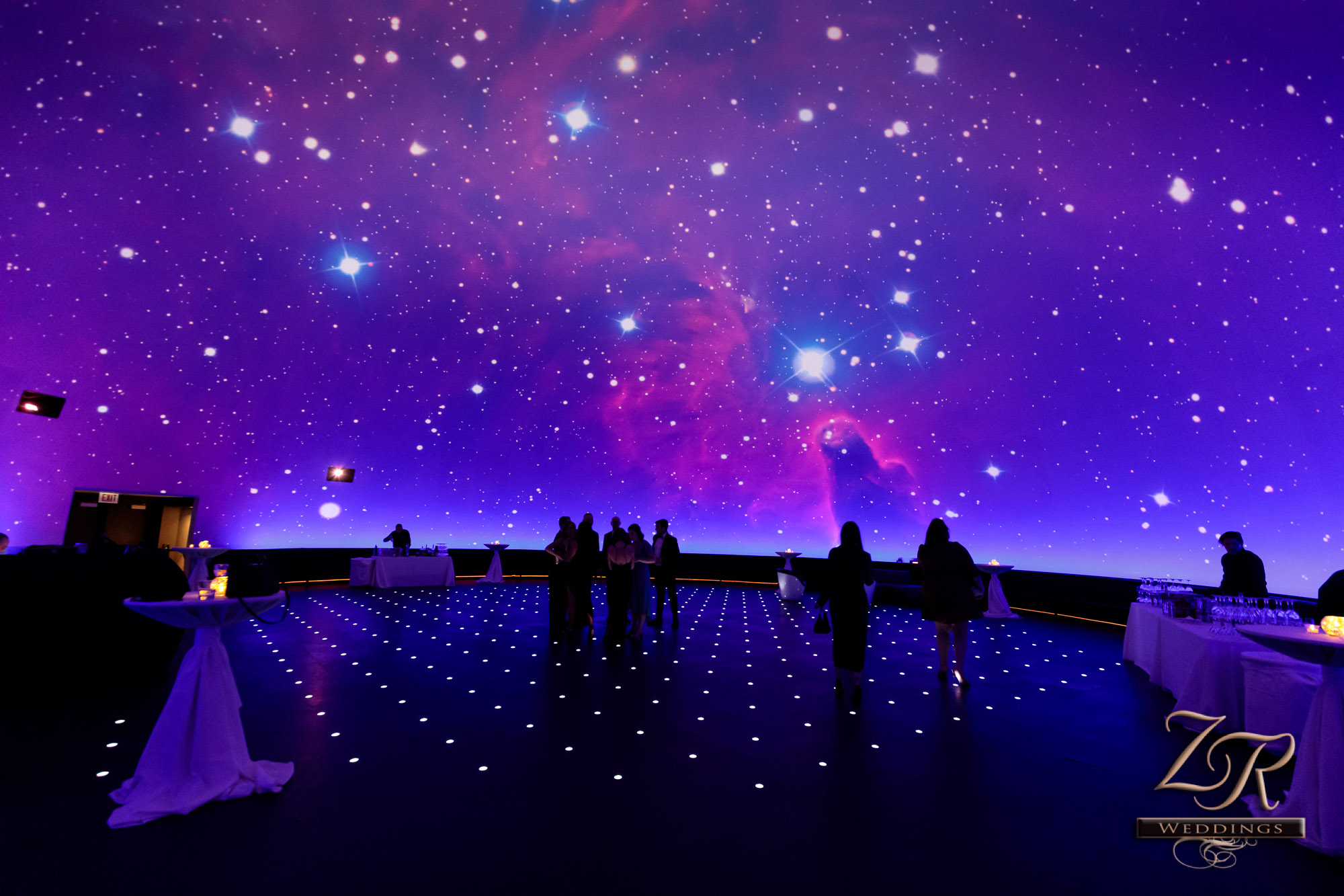 Celestial wallpaper with pinks, blues and purples in the Grainger Sky Theater set up for a wedding with high boys, a bar and a few people scattered around. ZR Weddings Photo Credit